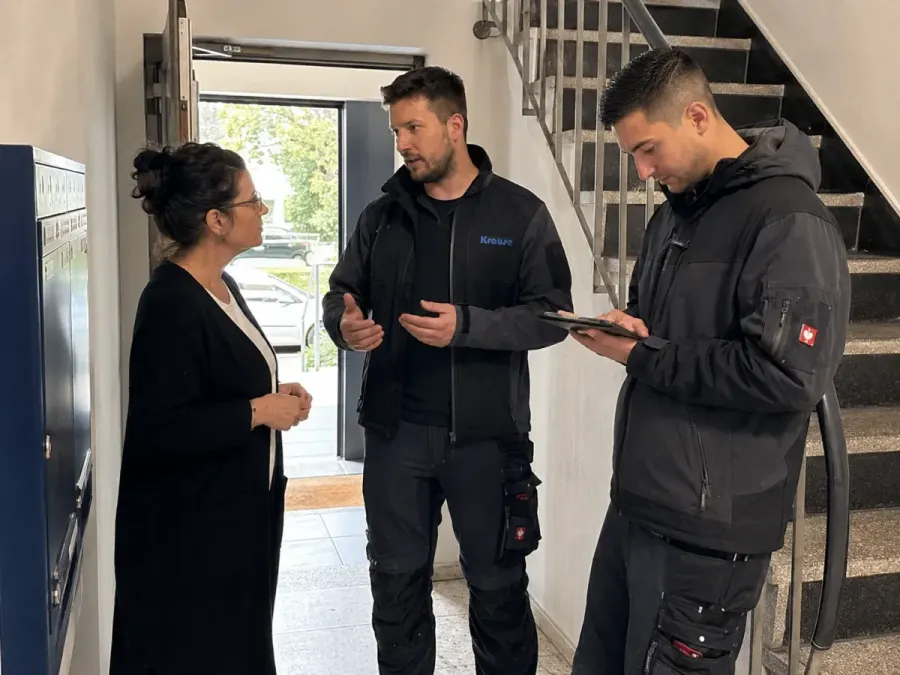 Zwei Krause-Fachkräfte besprechen mit einer Verwalterin den Auftrag im Treppenhaus